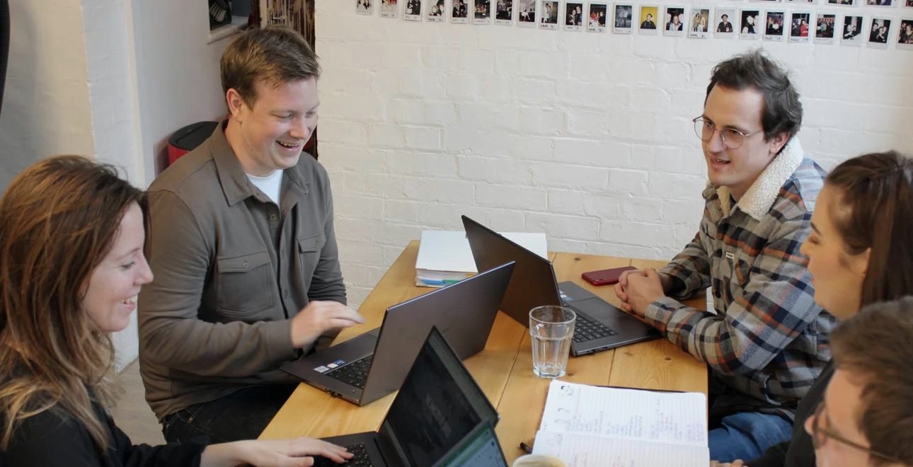 Colleagues work together on laptops around a shared table.