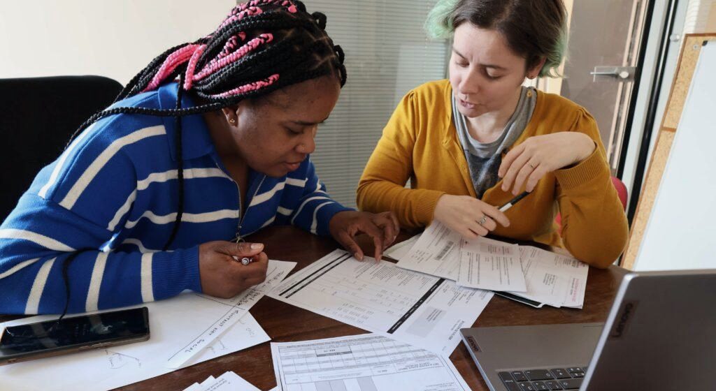 Two colleagues review printed documents together at a desk.